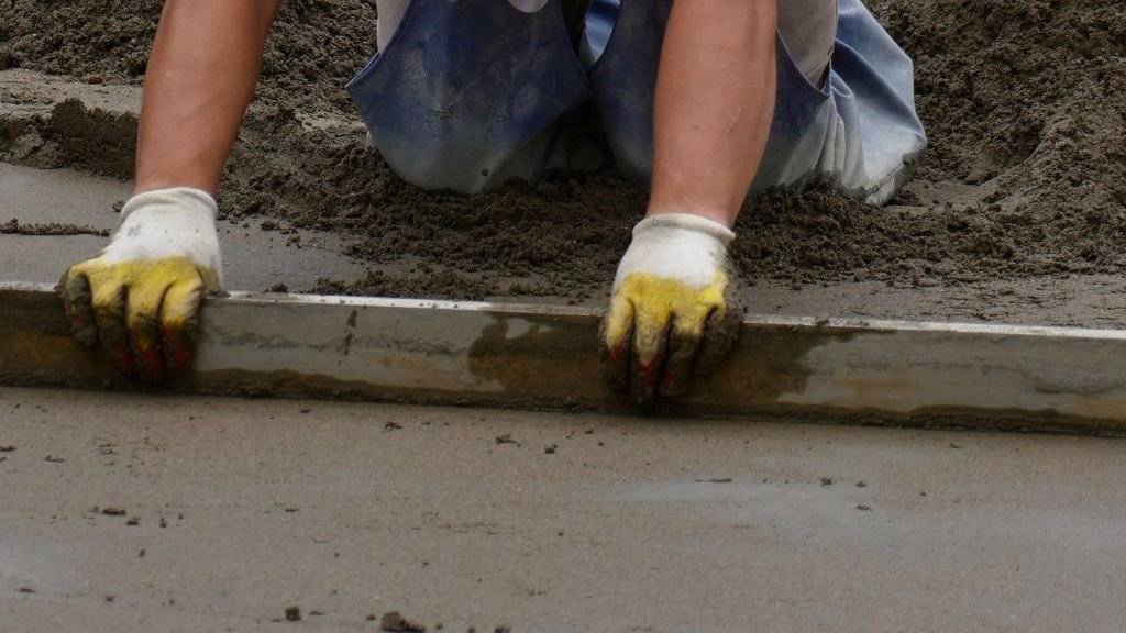 Construction worker leveling wet concrete with a straightedge screed during slab installation for an on-demand concrete project.